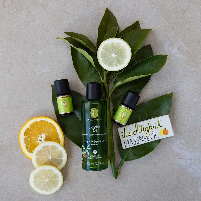 Ingredients for the DIY recipe: Essential Oils ,Orange org. , Lemon org., Organic Jojoba Oil , and the “Lightness Massage Oil” label. In the background are slices of citrus fruit and green leaves.