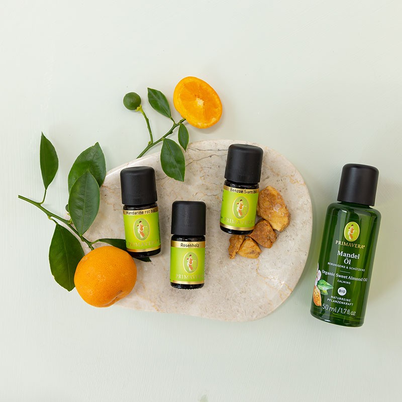 Ätherischer Öle Benzoe Siam, Mandarine und Rosenholz mit PRIMAVERA Mandelöl auf einer Steinschale, dekorativ arrangiert mit frischen Mandarinenzweigen.