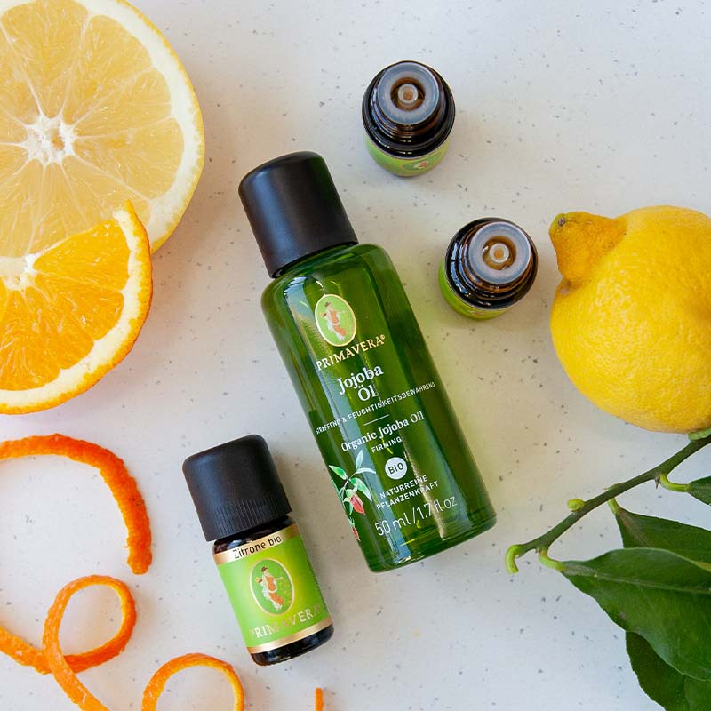 Weißer Teller mit Zitrone, Zitrusscheiben, Jojobaöl bio, Orangenöl bio, Grapefruitöl bio und Zitrone bio.