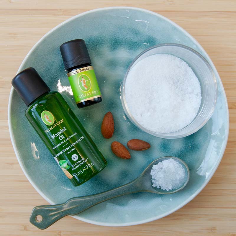 Grüner Teller mit PRIMAVERA Mandelöl und Yuzu Zitrone, einer kleinen Schale Salz mit Löffel und drei Mandelkerne.