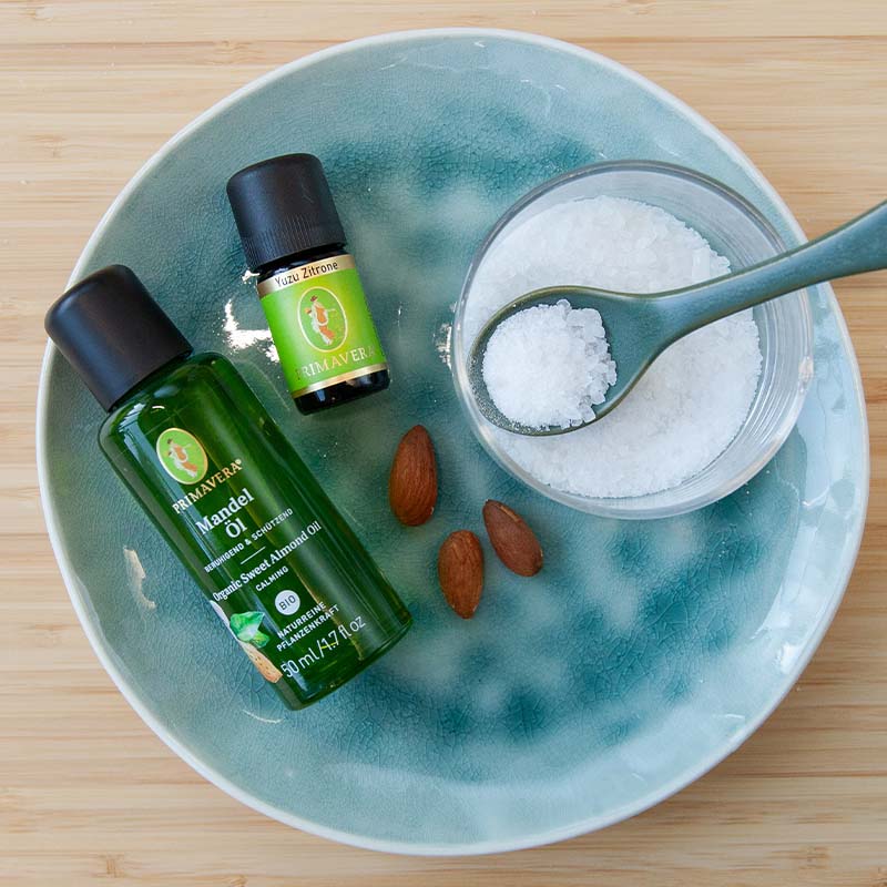 Grüner Teller mit PRIMAVERA Mandelöl und Yuzu Zitrone, einer kleinen Schale Salz mit Löffel und drei Mandelkerne.