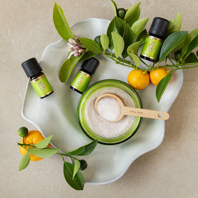 Zutaten für ein DIY‑Badesalz mit ätherischen Ölen und Zitrusfrüchten auf einer Schale.