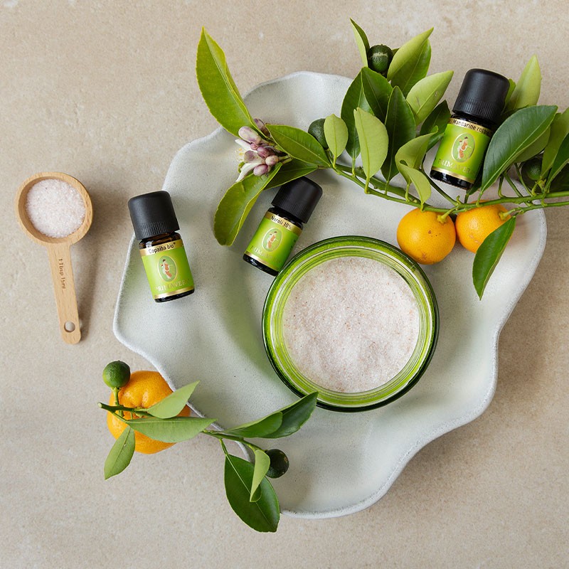 Zutaten für ein DIY‑Badesalz mit ätherischen Ölen und Zitrusfrüchten auf einer Schale.