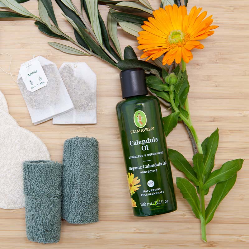 PRIMAVERA Ringelblumenöl, Teebeutel, gewaschene Stoffstücke, Calendula Blüten und Blätter schön dekoriert auf einem Holzuntergrund