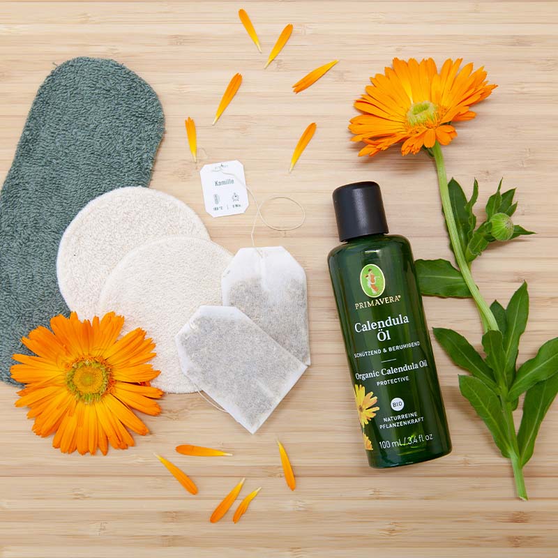 PRIMAVERA Ringelblumenöl, Teebeutel, gewaschene Stoffkreise, Calendula Blüten und Blätter schön dekoriert auf einem Holzuntergrund