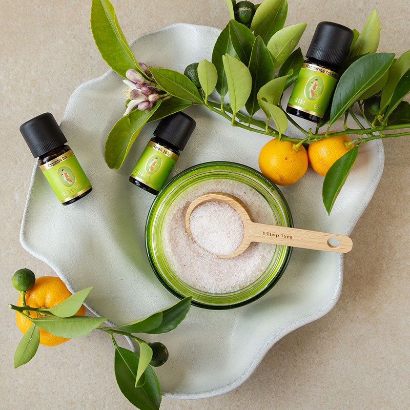 Zutaten für ein DIY‑Badesalz mit ätherischen Ölen und Zitrusfrüchten auf einer Schale.