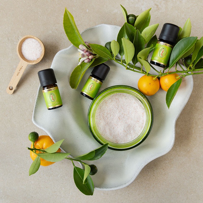 Zutaten für ein DIY‑Badesalz mit ätherischen Ölen und Zitrusfrüchten auf einer Schale.