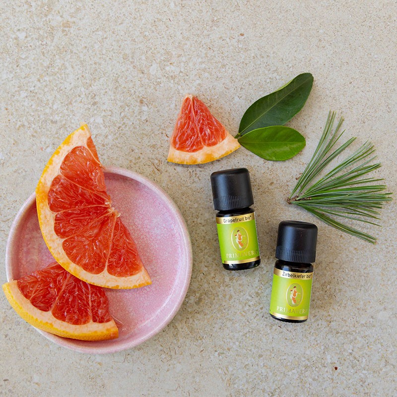 Grapefruit bio und Zirbelkiefer bio auf einem Tisch mit einem Teller Grapefruitscheiben und Kiefernadeln