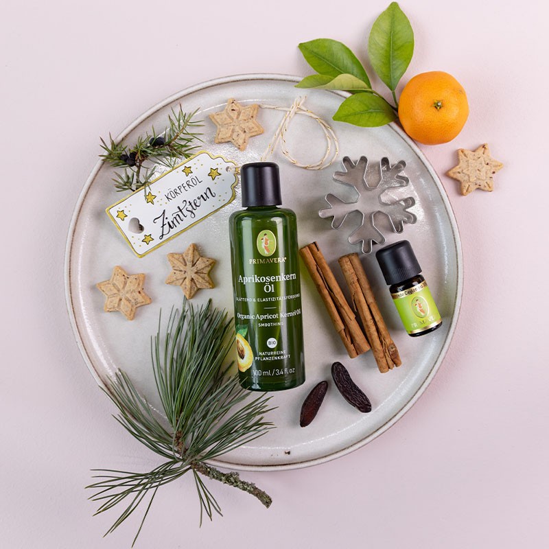 Primavera Aprikosenkernöl und ätherisches Öl auf rundem Tablett, dekoriert mit Zimtstangen, Sternplätzchen, Tannenzweig, Tonkabohnen und Mandarine.