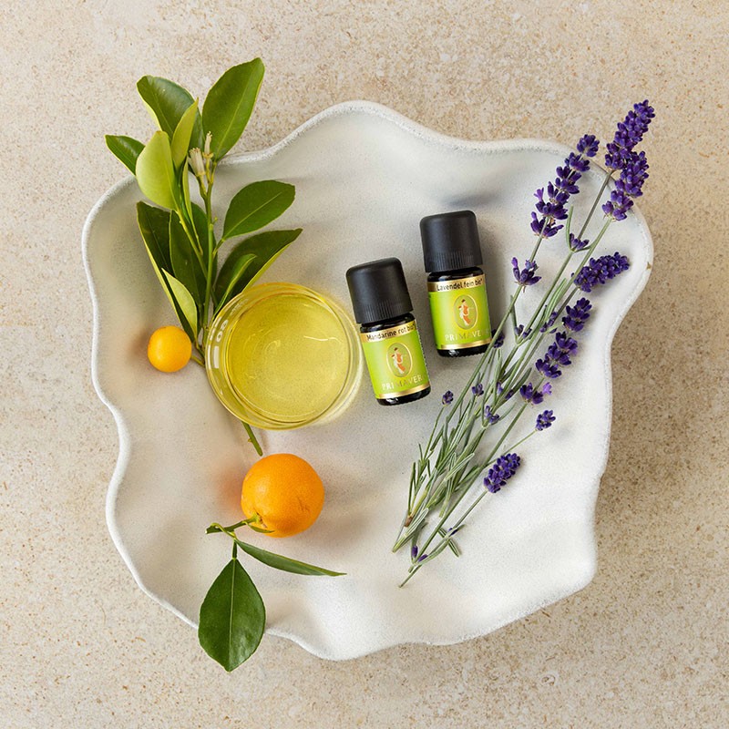 Mandarine rot bio, Lavendel fein bio und eine Schale Massageöl auf einem Teller verziert mit Mandarinen und Lavendel.