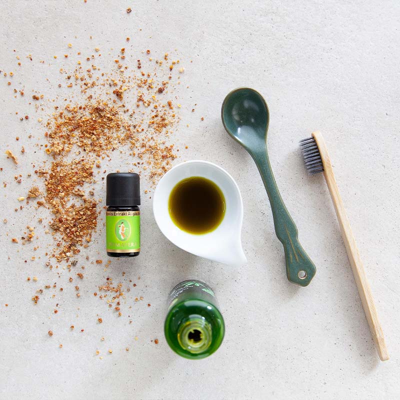 Ätherisches Öl Propolis Extrakt bio, weiße Schale mit Hanfsamenöl bio, grüner Löffel, Holzzahnbürste und Propolis auf heller Fläche.