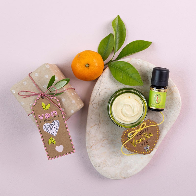 Die Fertige Sheasahne auf einem Steinteller mit den Ätherischen Vanilleextrakt, dekoriert mit einem kleinem Geschenk, einer Orange und eine Luftschlange.