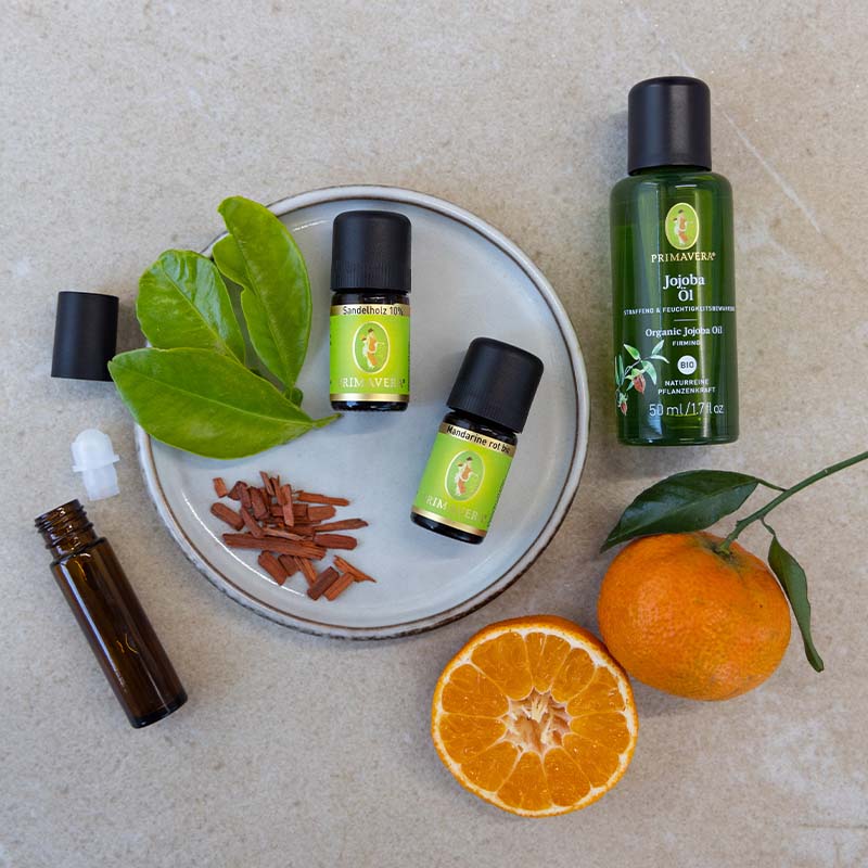 Ätherische Öl Fläschchen, Mandarine rot bio, Jojobaöl bio, leere Roll-On Flasche mit Holzspänen und Mandarinen dekorativ arrangiert.