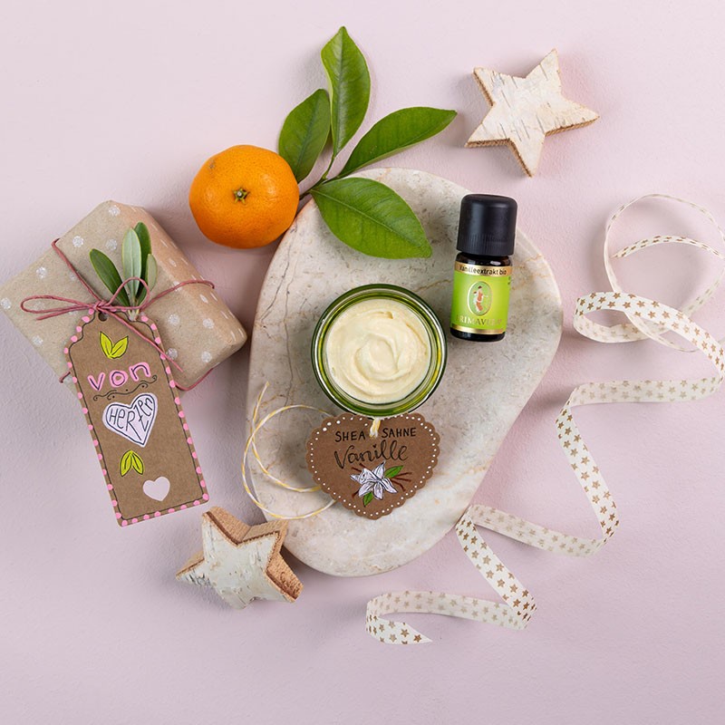 Die Fertige Sheasahne auf einem Steinteller mit den Ätherischen Vanilleextrakt, dekoriert mit einem kleinem Geschenk, einer Orange und eine Luftschlange.