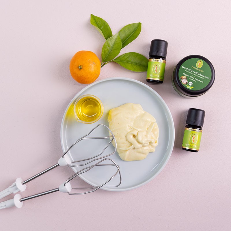 Auf einem Teller ist die Sheasahne die gerade Zubereitet wird, die Zutaten die Verwendet werden stehen daneben, auf dem Teller liegen Schneebesen Aufsetzer für ein Elektrisches Rührgerät. 